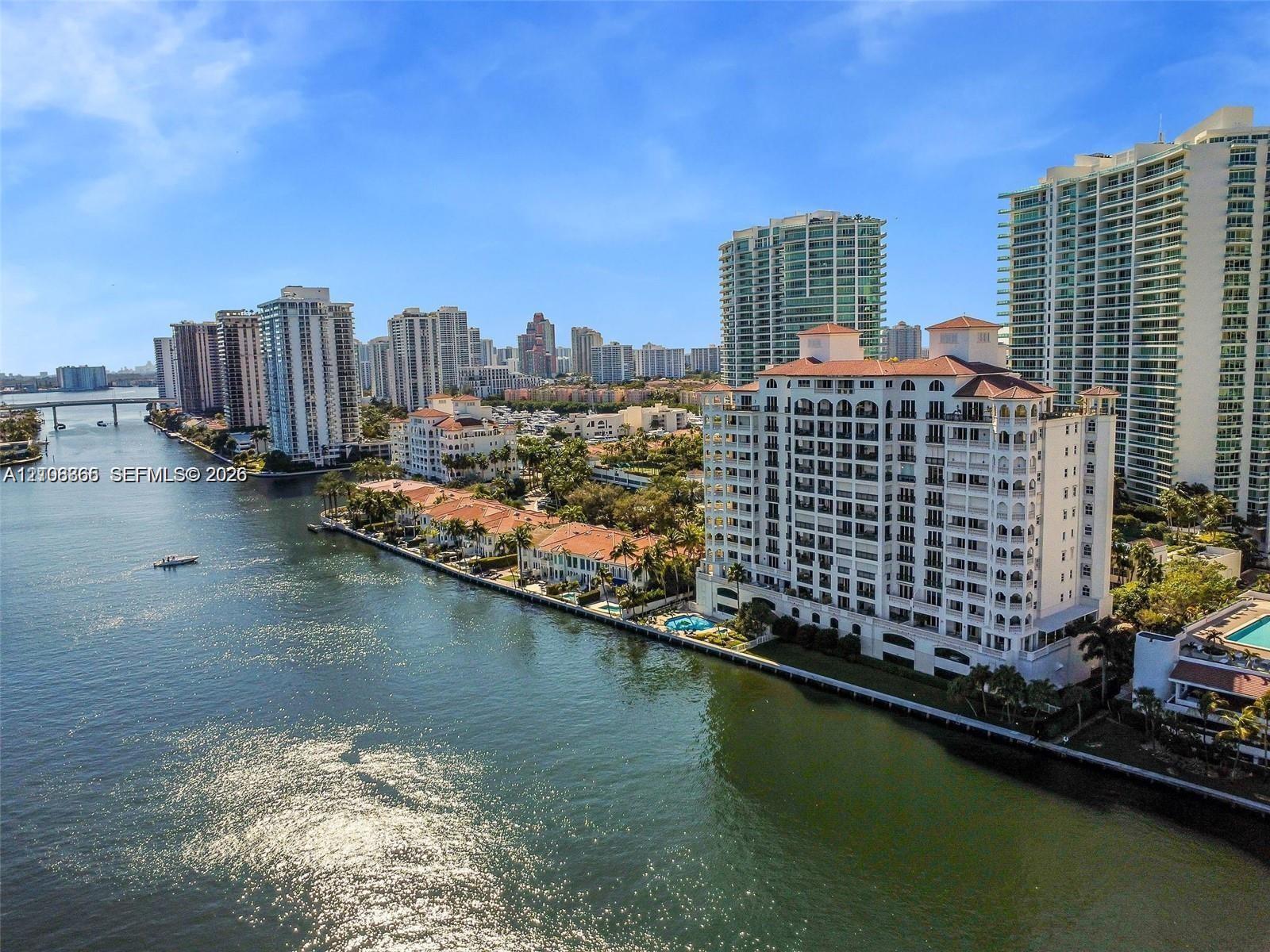 Waterfront high-rise building featuring a red-tiled roof, multi-level balconies, and a ground-level swimming pool