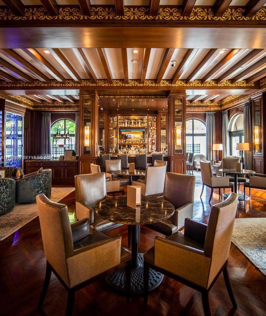 Ornate wood-paneled lounge featuring an intricate coffered ceiling with gold-leaf detailing, polished wood-finish flooring, built-in bar cabinetry, and arched windows