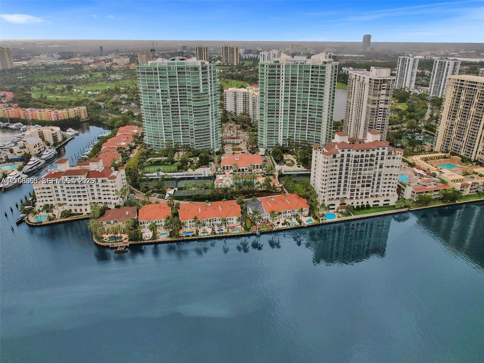 Waterfront residential complex featuring high-rise towers, multi-level structures with red-tiled roofs, integrated swimming pools, and tennis courts Waterfront residential complex featuring high-rise towers, multi-level structures with red-tiled roofs, integrated swimming pools, and tennis courts