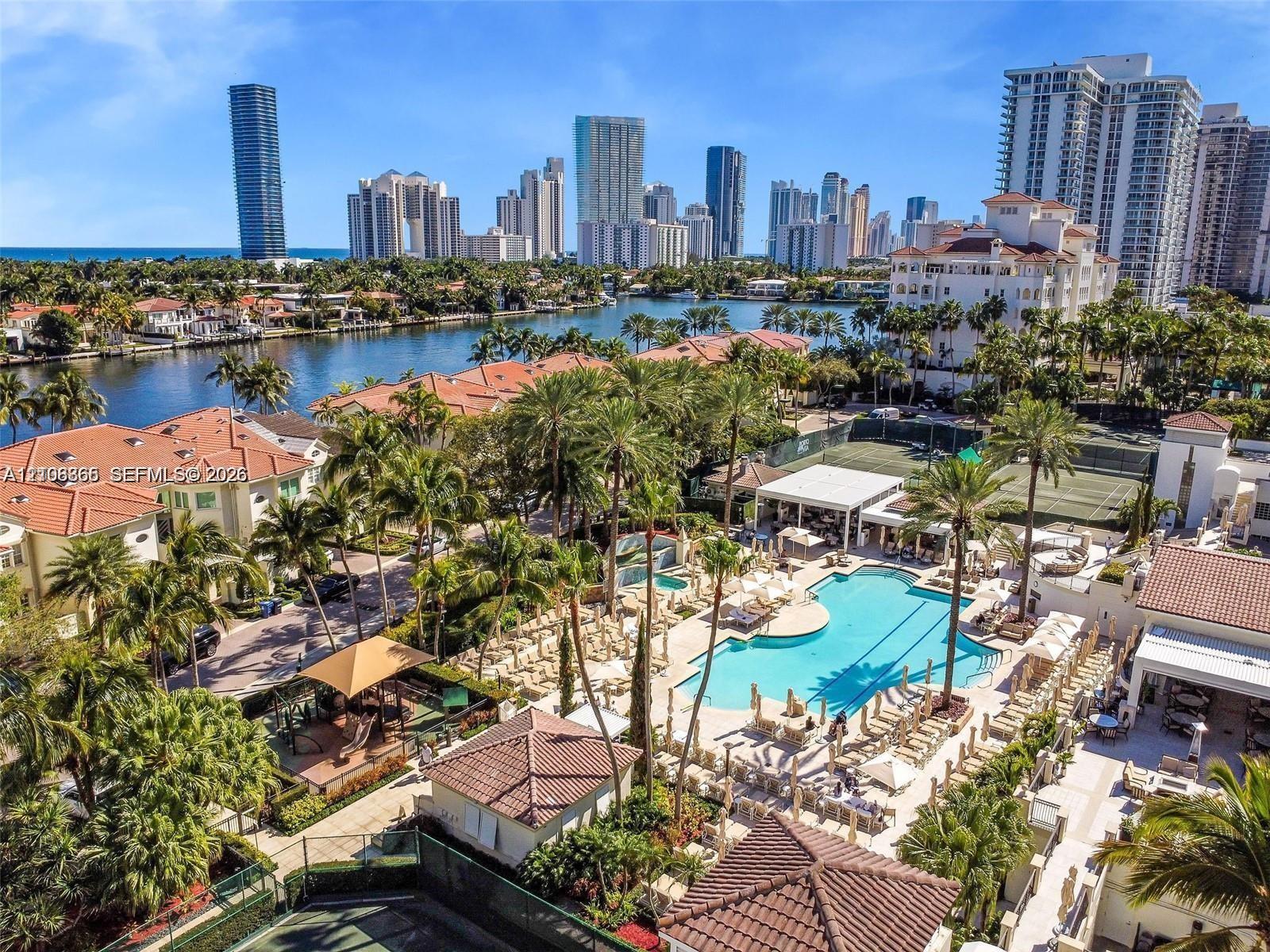Waterfront community featuring an expansive swimming pool, professional-grade tennis courts, mature tropical landscaping, and tile-roof architecture Waterfront community featuring an expansive swimming pool, professional-grade tennis courts, mature tropical landscaping, and tile-roof architecture
