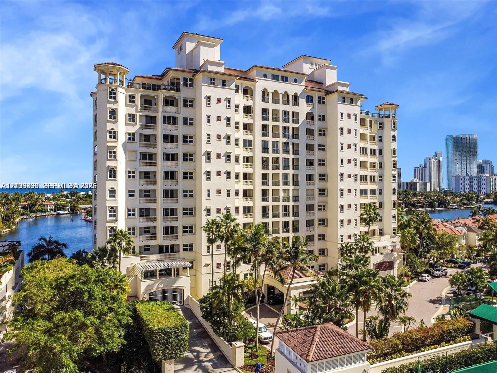 Mid-rise waterfront high-rise building featuring multi-level balconies, arched architectural detailing, a clay tile roof, and porte-cochre entry