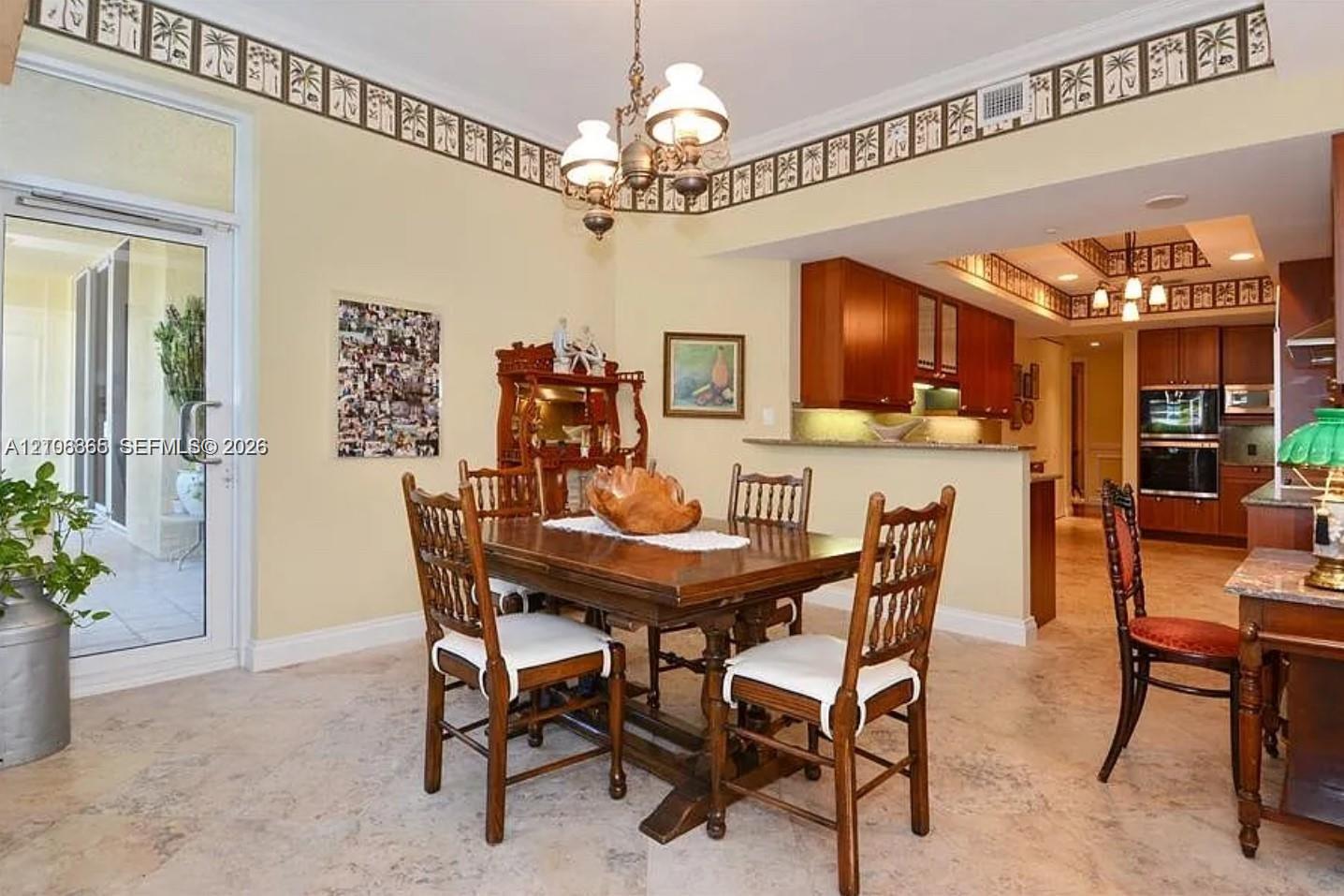 Open-concept dining area featuring stone tile flooring, stained wood cabinetry, recessed lighting, a decorative chandelier, and a full-glass exterior door
