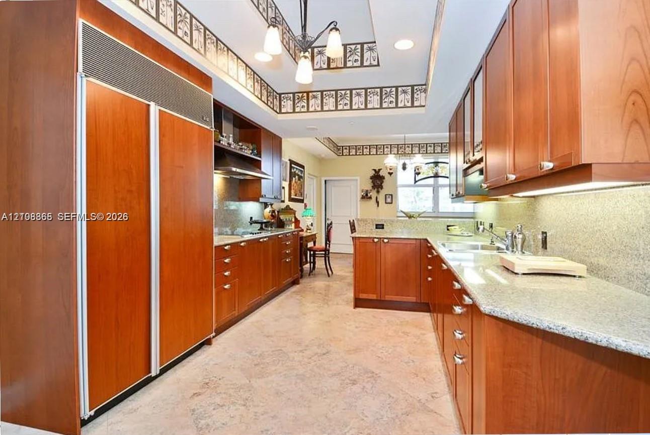Kitchen featuring custom wood cabinetry, integrated full-height refrigerator, stone countertops, stainless steel undermount sink, and stone tile flooring
