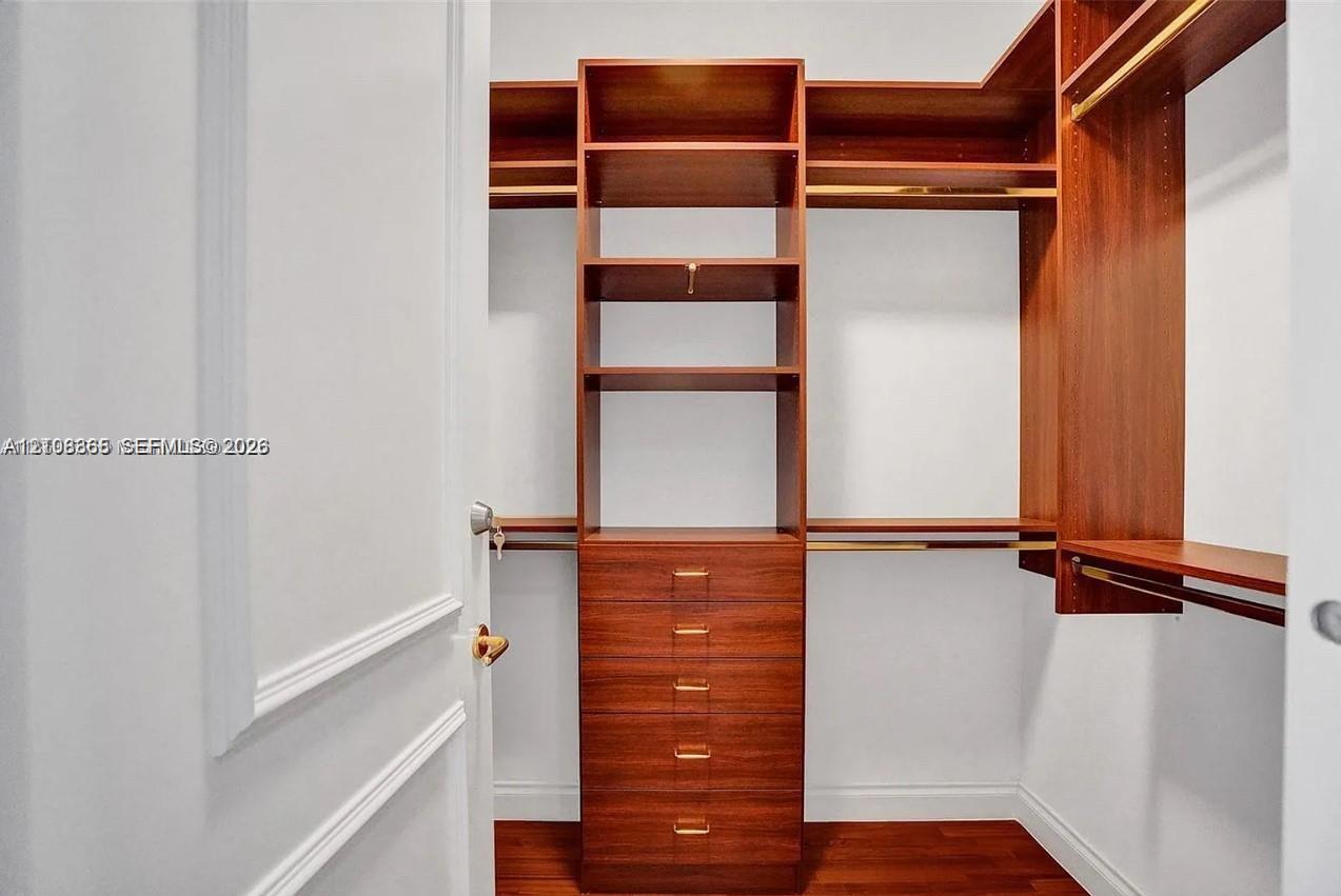 Custom walk-in closet featuring wood-finish cabinetry, built-in shelving, integrated dresser drawers, and metal hanging rods
