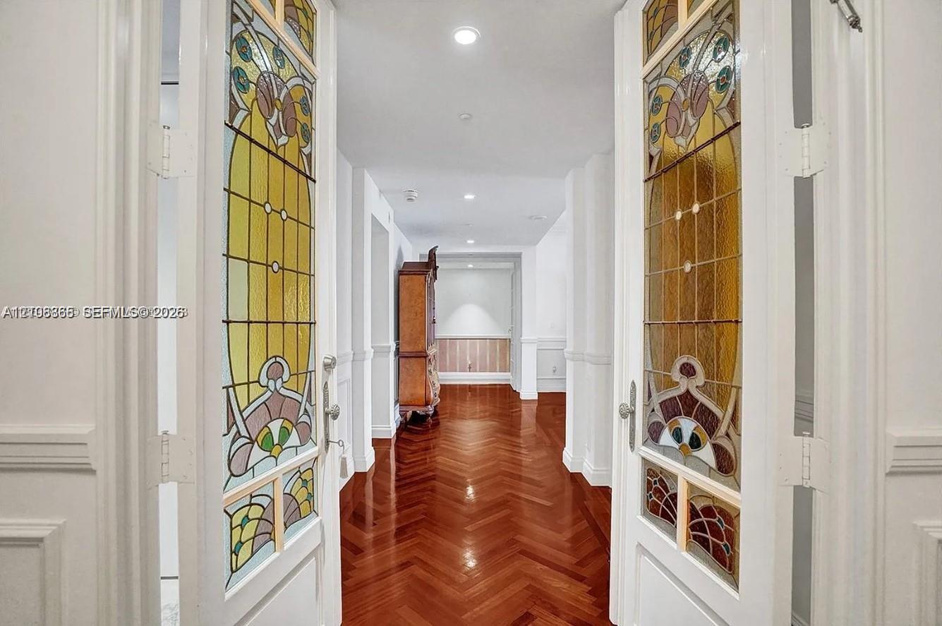 Double doors featuring decorative stained-glass panels, wood-finish flooring laid in a herringbone pattern, wainscoting, and recessed ceiling lighting Double doors featuring decorative stained-glass panels, wood-finish flooring laid in a herringbone pattern, wainscoting, and recessed ceiling lighting