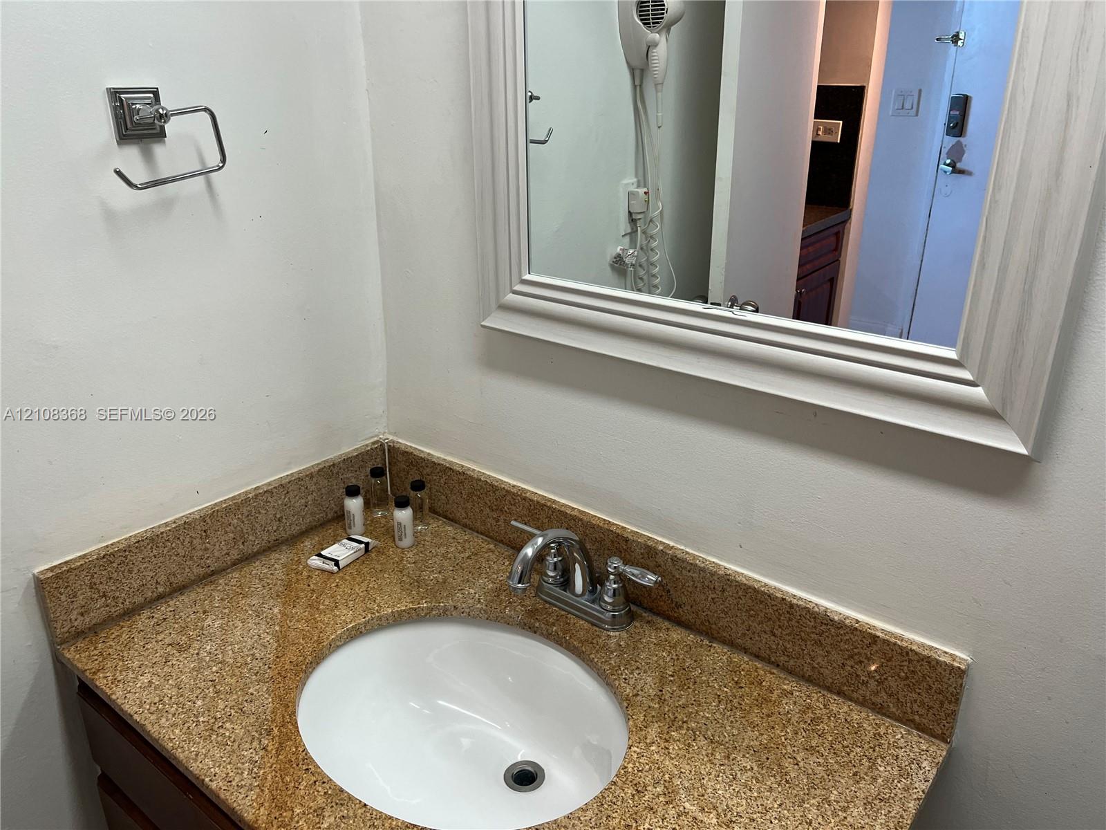 Vanity featuring a stone-composite countertop with an integrated undermount sink, chrome double-handle faucet, and a wall-mounted framed mirror