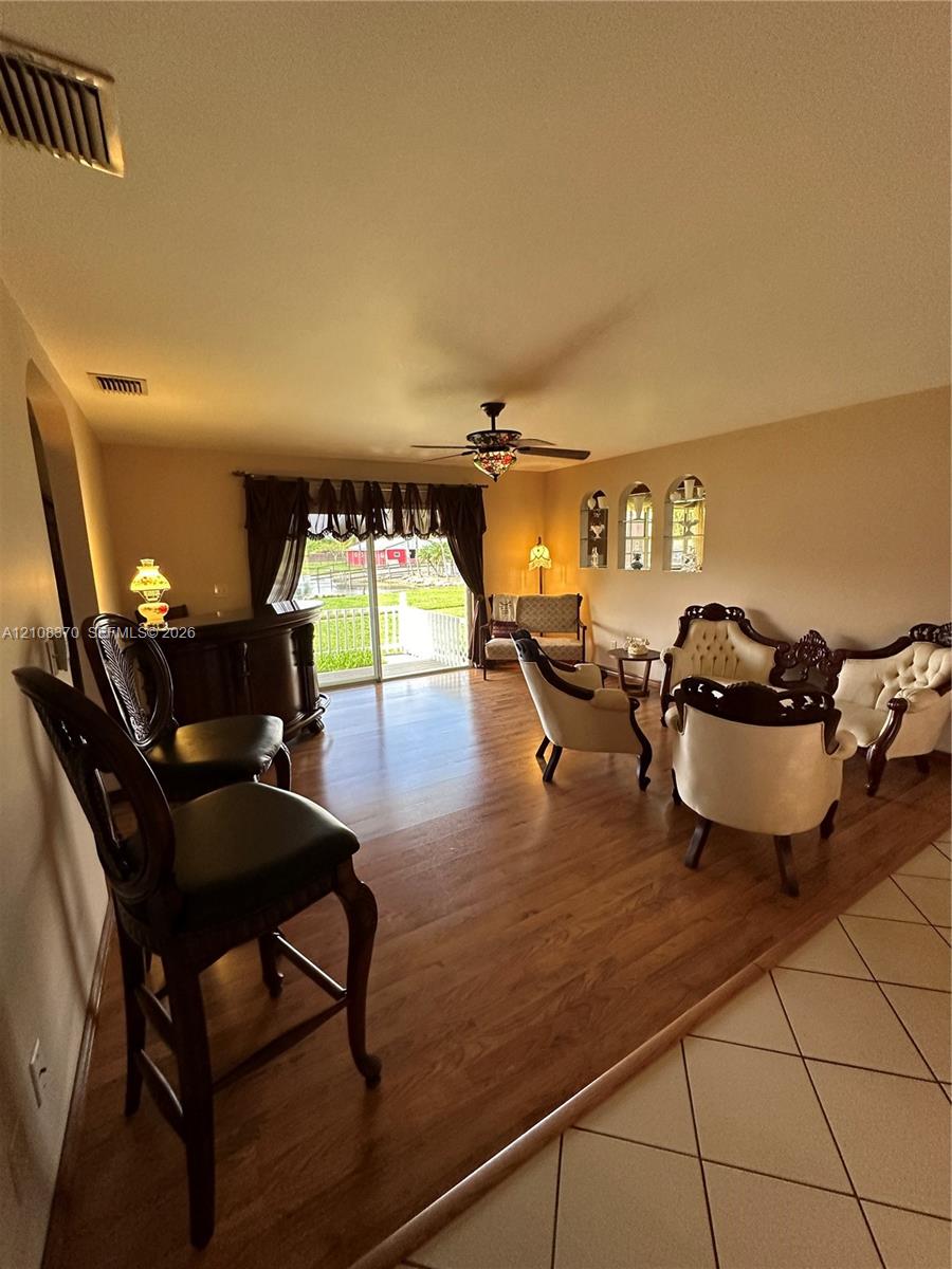 Living area featuring wood-finish flooring, built-in wet bar, arched wall niches, sliding glass door, and a ceiling fan