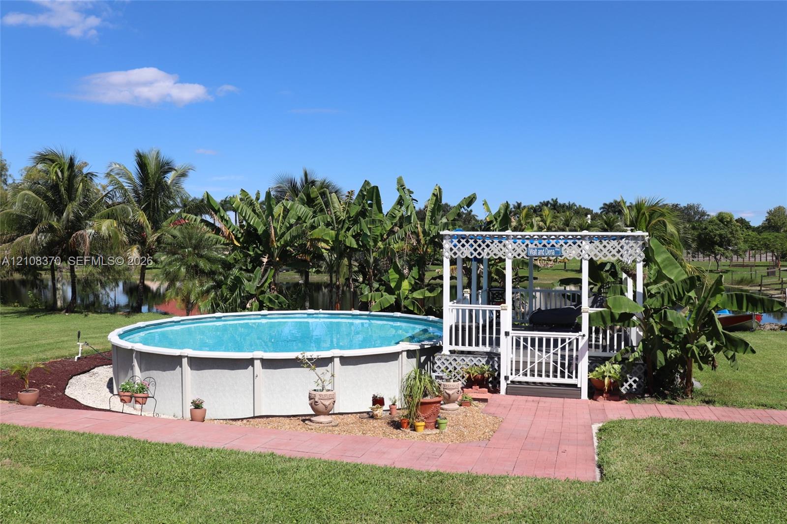 Above-ground swimming pool with surrounding gravel landscaping, accompanied by a white lattice-covered gazebo featuring an integrated deck and gate
