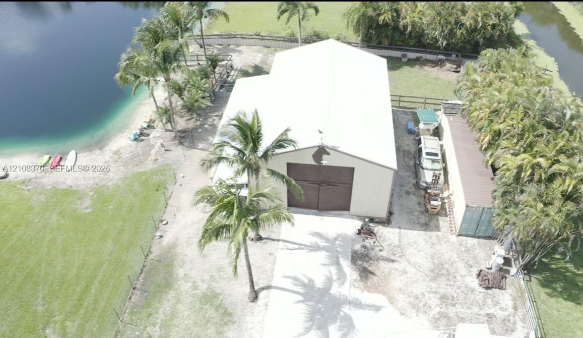 Detached metal workshop featuring dual sliding doors, a white exterior finish, concrete driveway, and direct water frontage on a landscaped lot