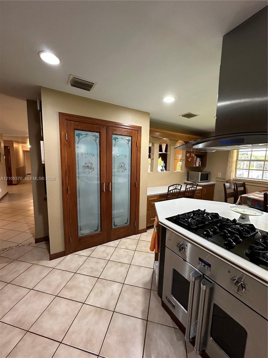 Double pantry with frosted glass paneled doors, stainless steel gas range with overhead ventilation hood, recessed lighting, and tile flooring