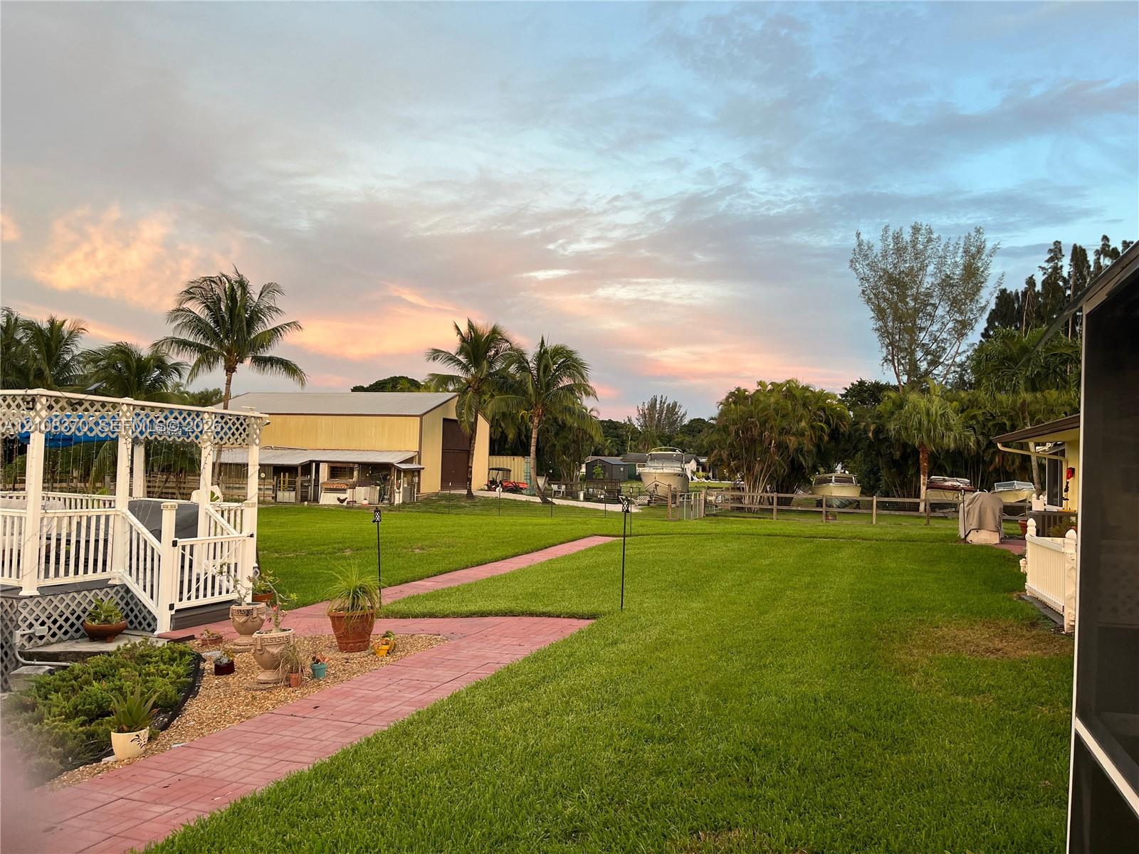 Expansive backyard featuring a manicured lawn, a paved stone walkway, a multi-level white wood-finish deck, and a detached metal-sided outbuilding