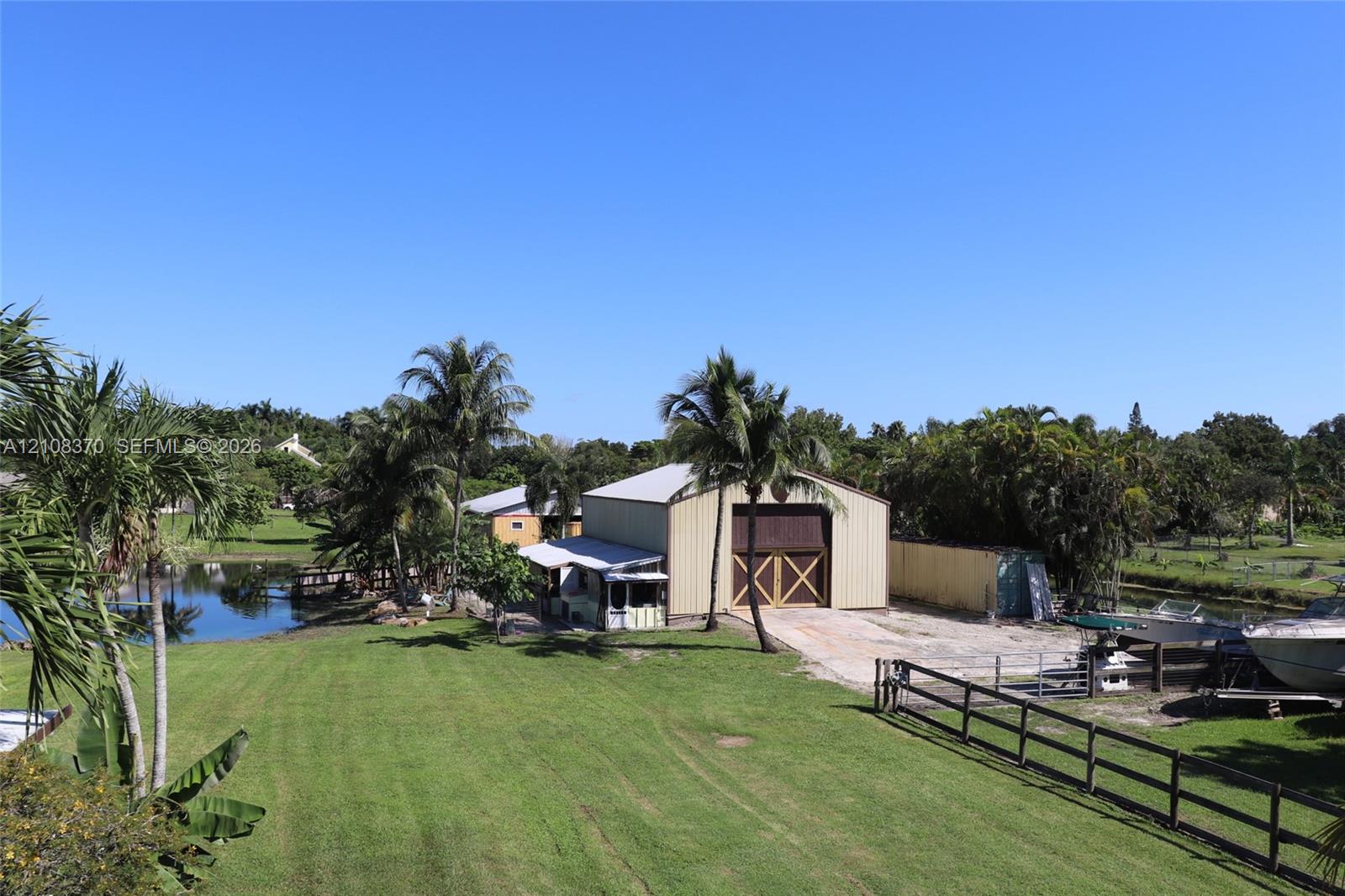 Expansive grounds featuring a metal-sided workshop with dual-entry doors, a grass lawn, mature palms, and bulkhead water access