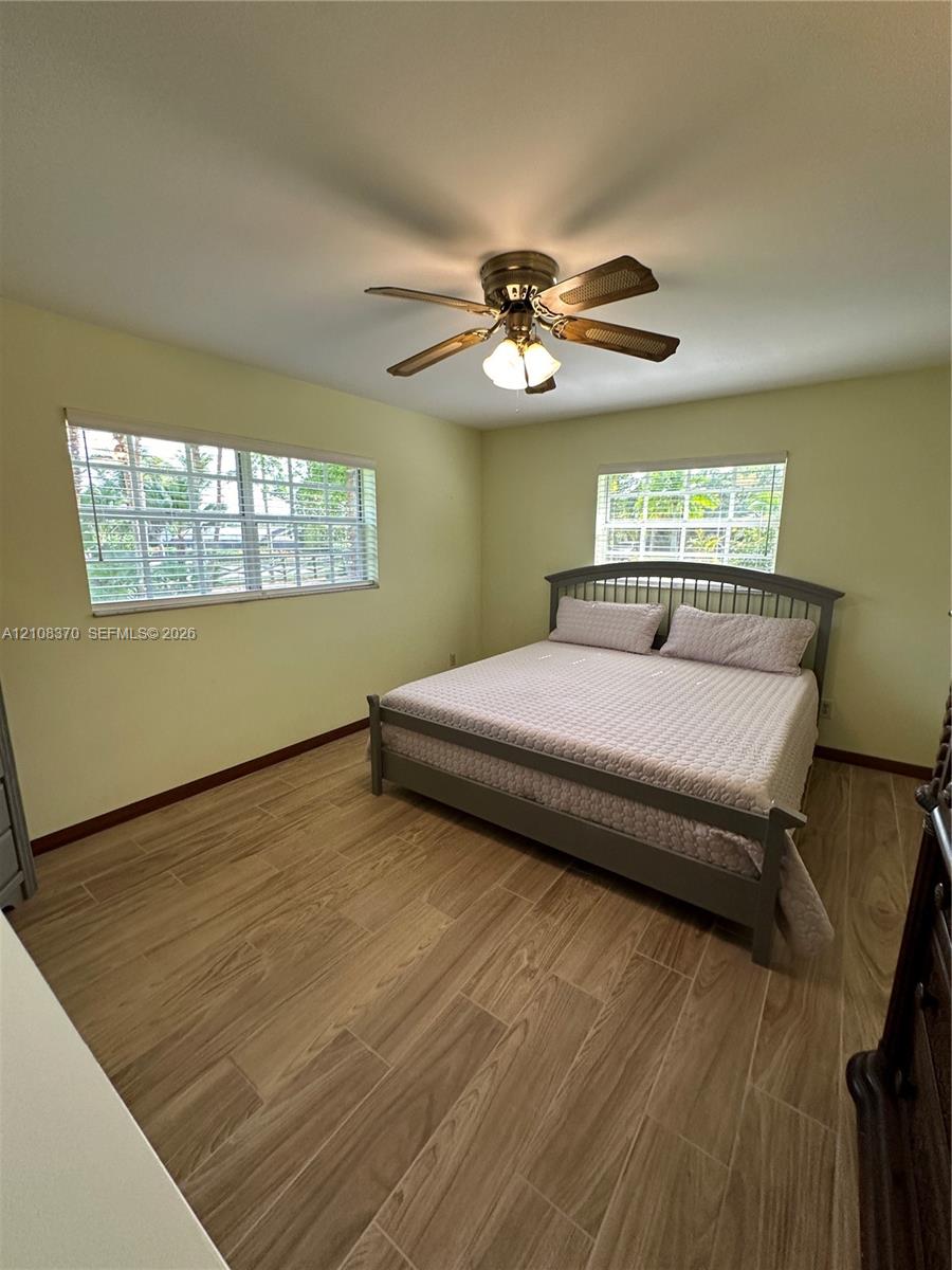 Interior space featuring wood-finish tile flooring, two windows with horizontal blinds, and a multi-blade ceiling fan with integrated lighting