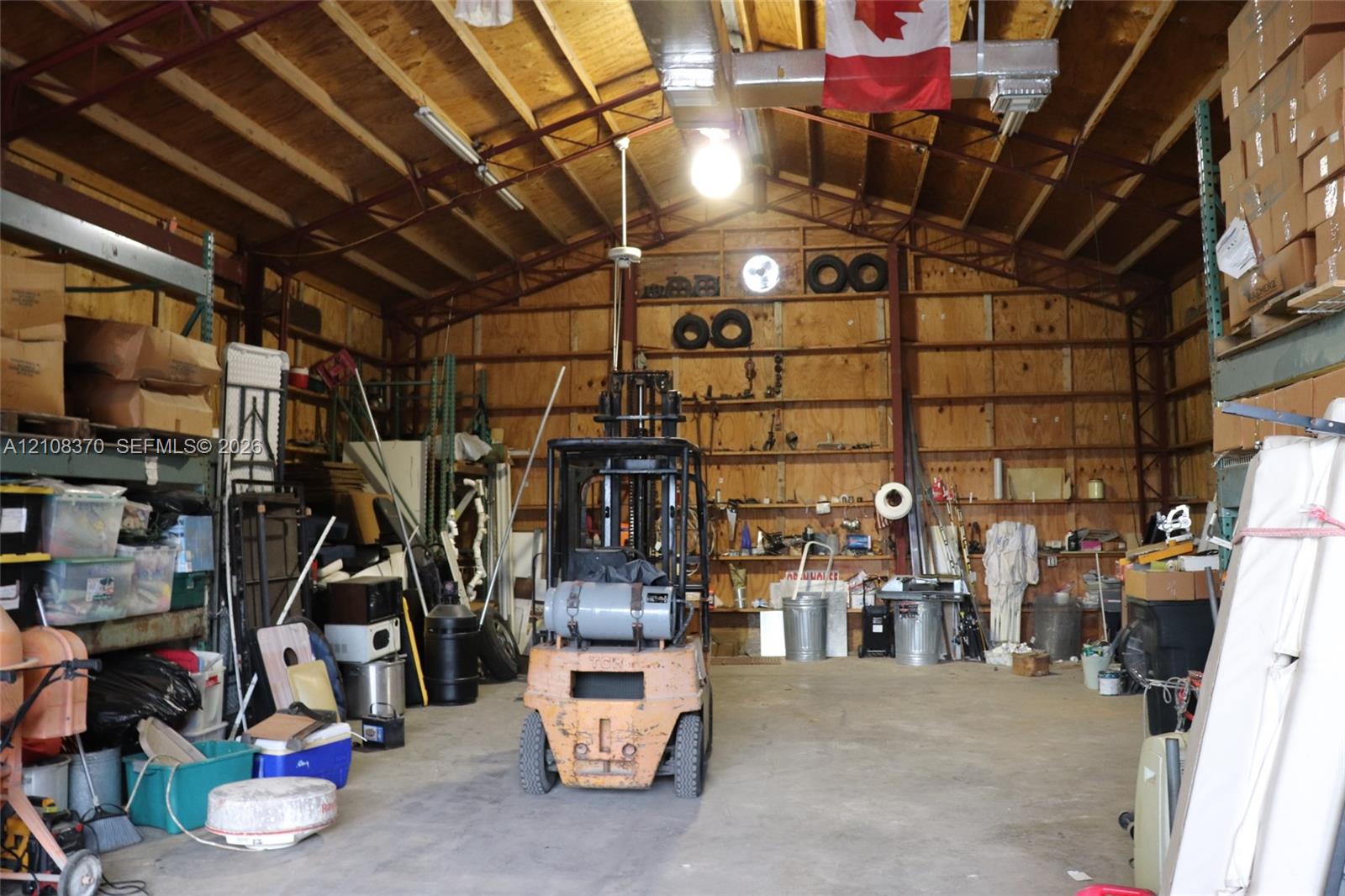 Spacious industrial-style workshop featuring high vaulted ceilings, exposed structural metal framing, reinforced concrete flooring, and extensive wall-mounted open shelving