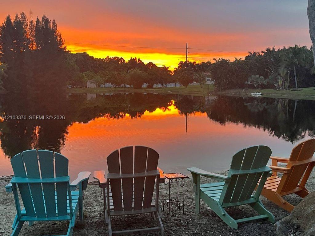 Waterfront property featuring a pond, mature trees, and a sunset backdrop