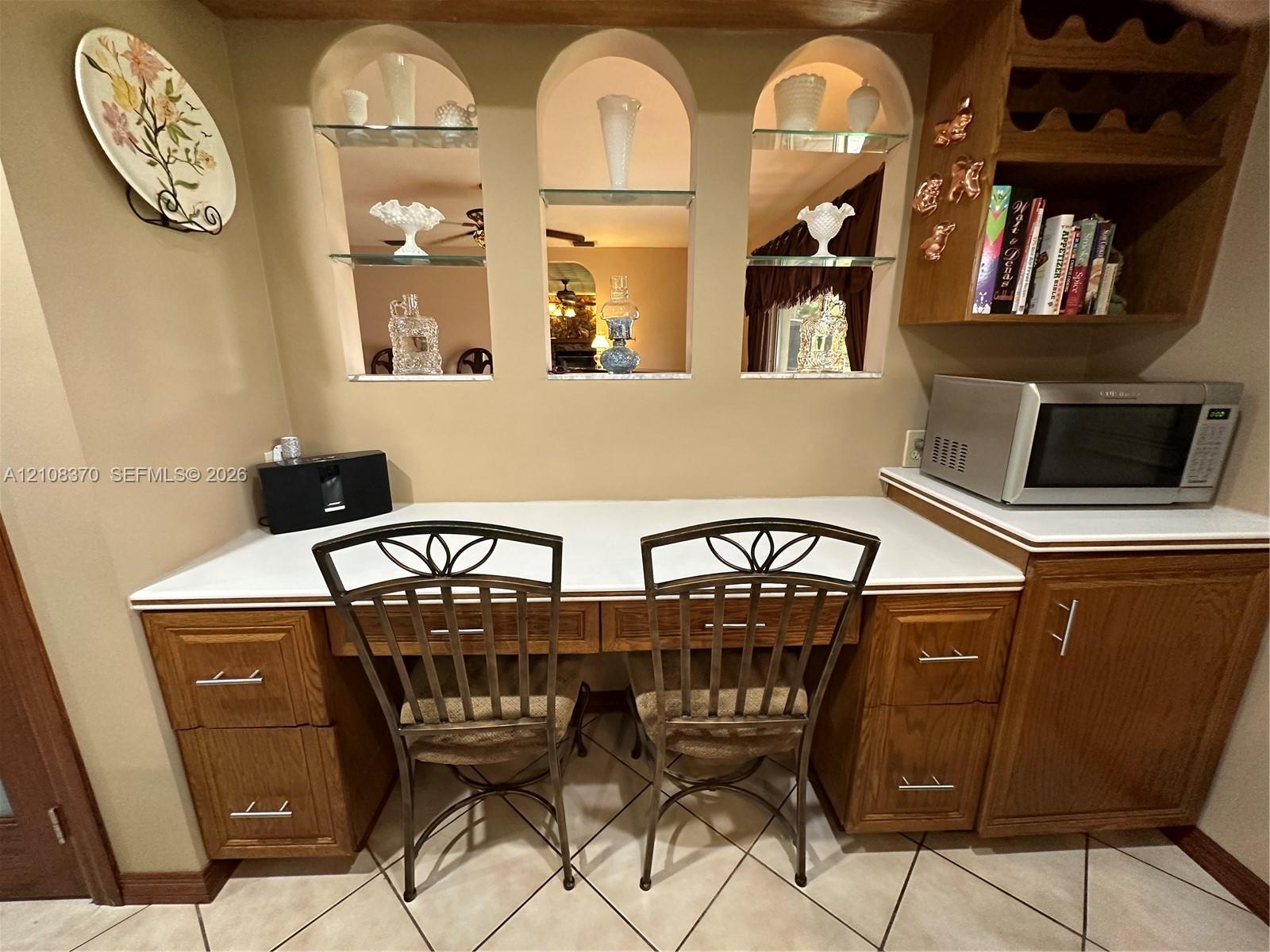 Built-in wood cabinetry featuring brushed nickel hardware, expansive solid-surface countertop, three arched display niches with glass shelving, and integrated wine storage