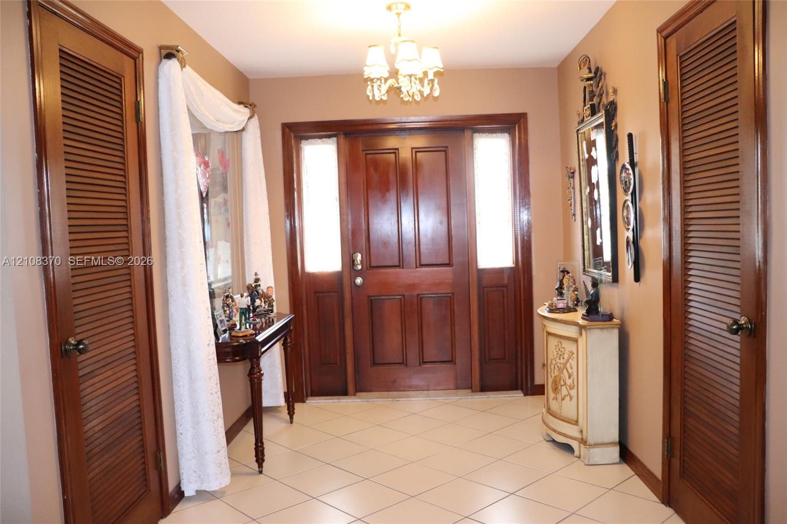 Foyer featuring a solid wood entry door with flanking sidelights, ceramic tile flooring, and dual wood-finished louvered closet doors