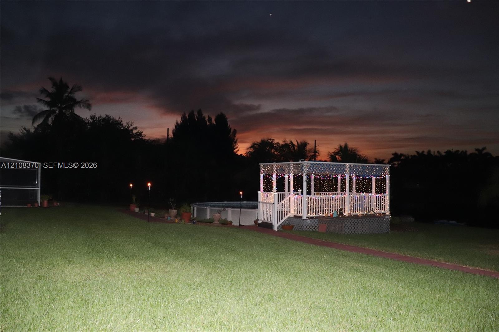 Backyard area featuring an elevated wooden gazebo, an above-ground pool, and a manicured lawn