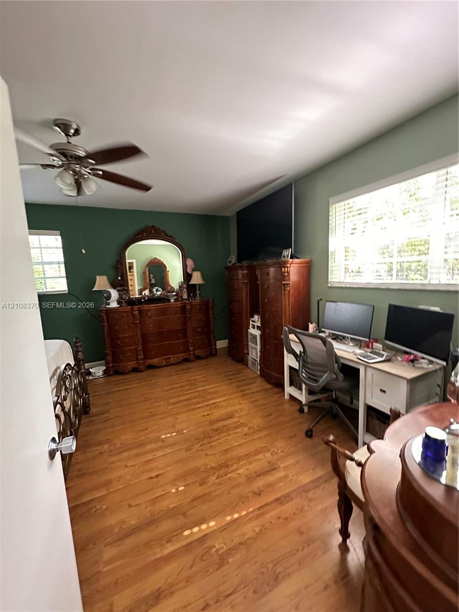 Wood-finish flooring, multi-blade ceiling fan with integrated lighting, and dual windows with horizontal blinds