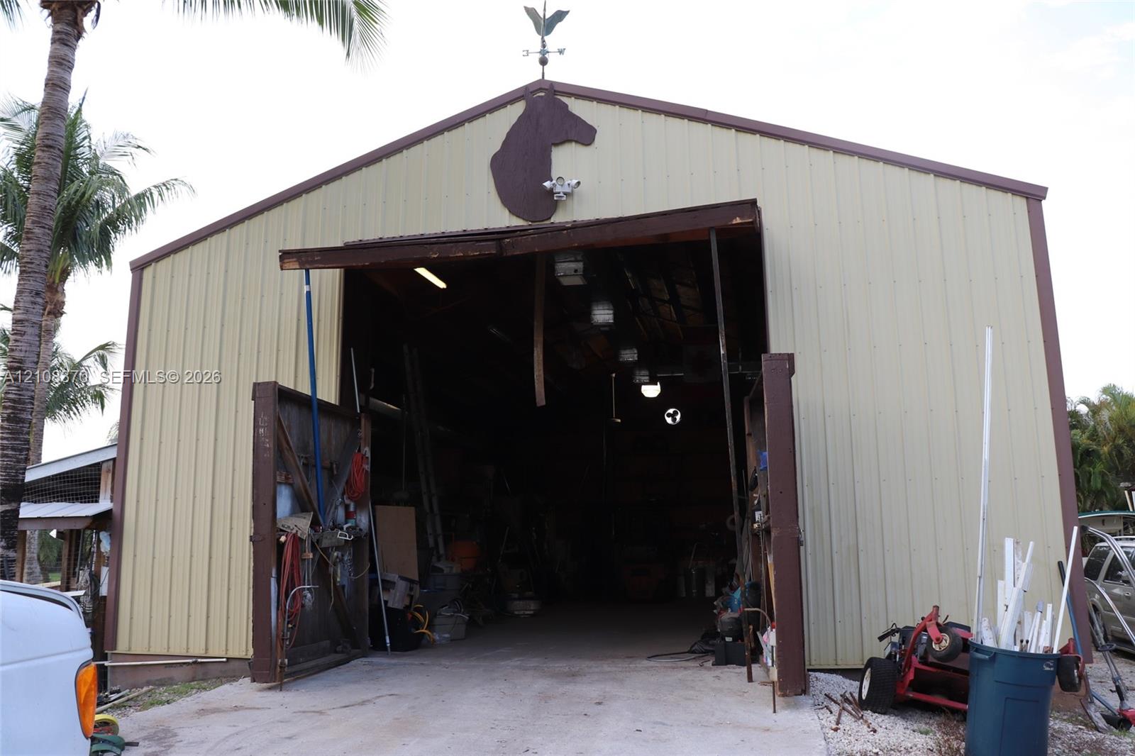 Metal-sided outbuilding featuring a high-clearance entrance, swinging door mechanisms, and a decorative roof-mounted weather vane