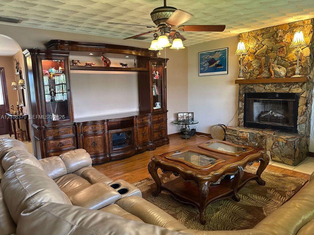 Living area featuring a floor-to-ceiling natural stone fireplace with a raised hearth, wood-finish flooring, built-in wooden media cabinetry, and a ceiling fan with integrated lighting