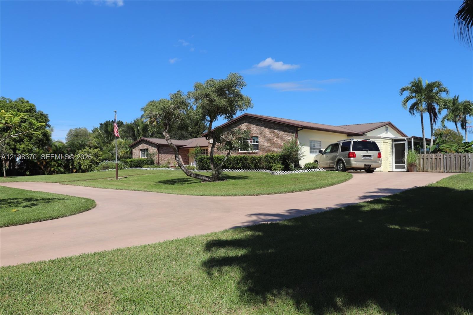 Single-story residence featuring a brick facade, multi-gabled roofline, sprawling manicured lawn, curved concrete driveway, and mature landscaping