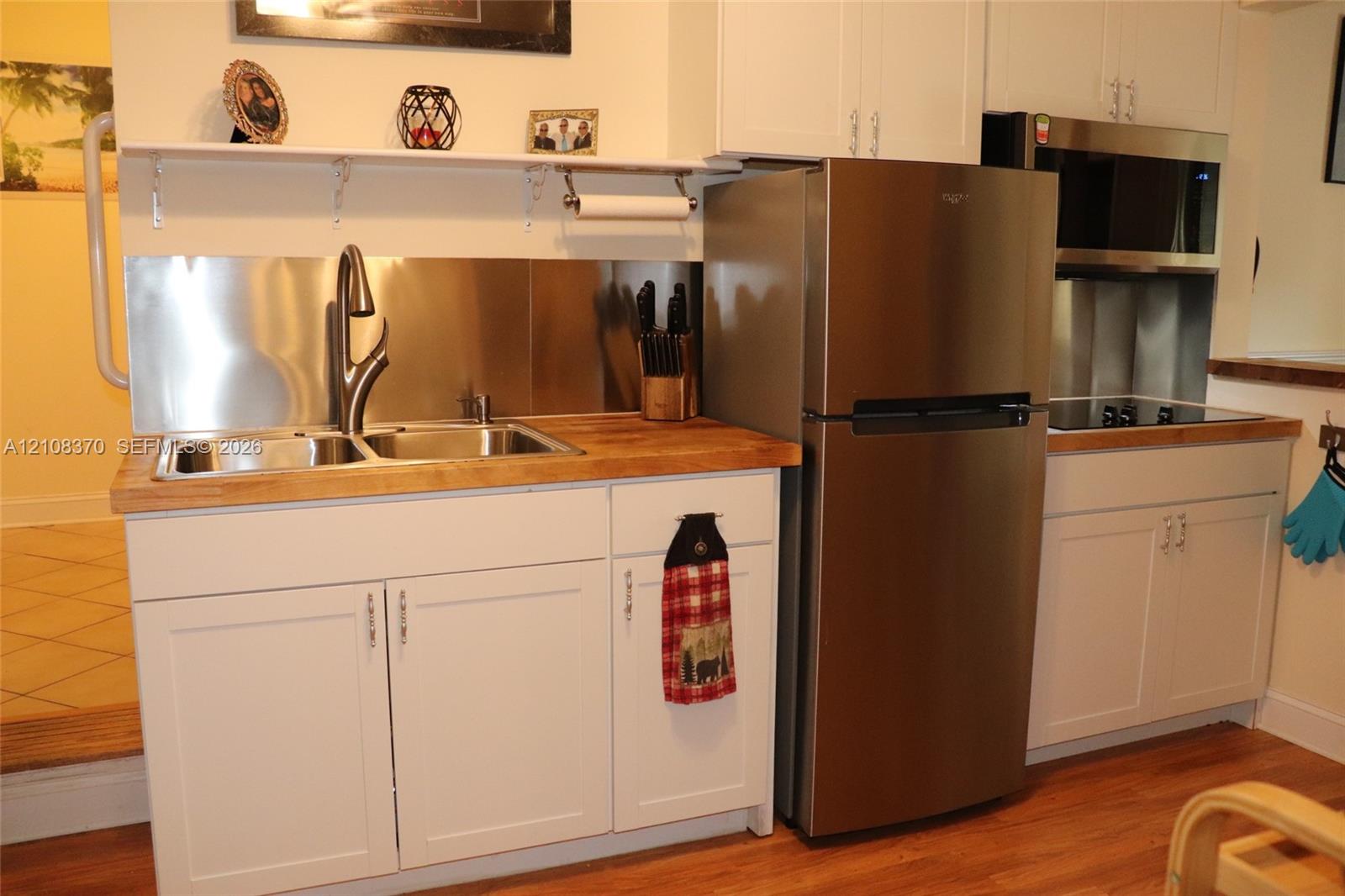 White shaker-style cabinetry, wood-surface countertops, stainless steel appliances, dual-basin stainless steel sink with high-arc faucet, and stainless steel backsplash