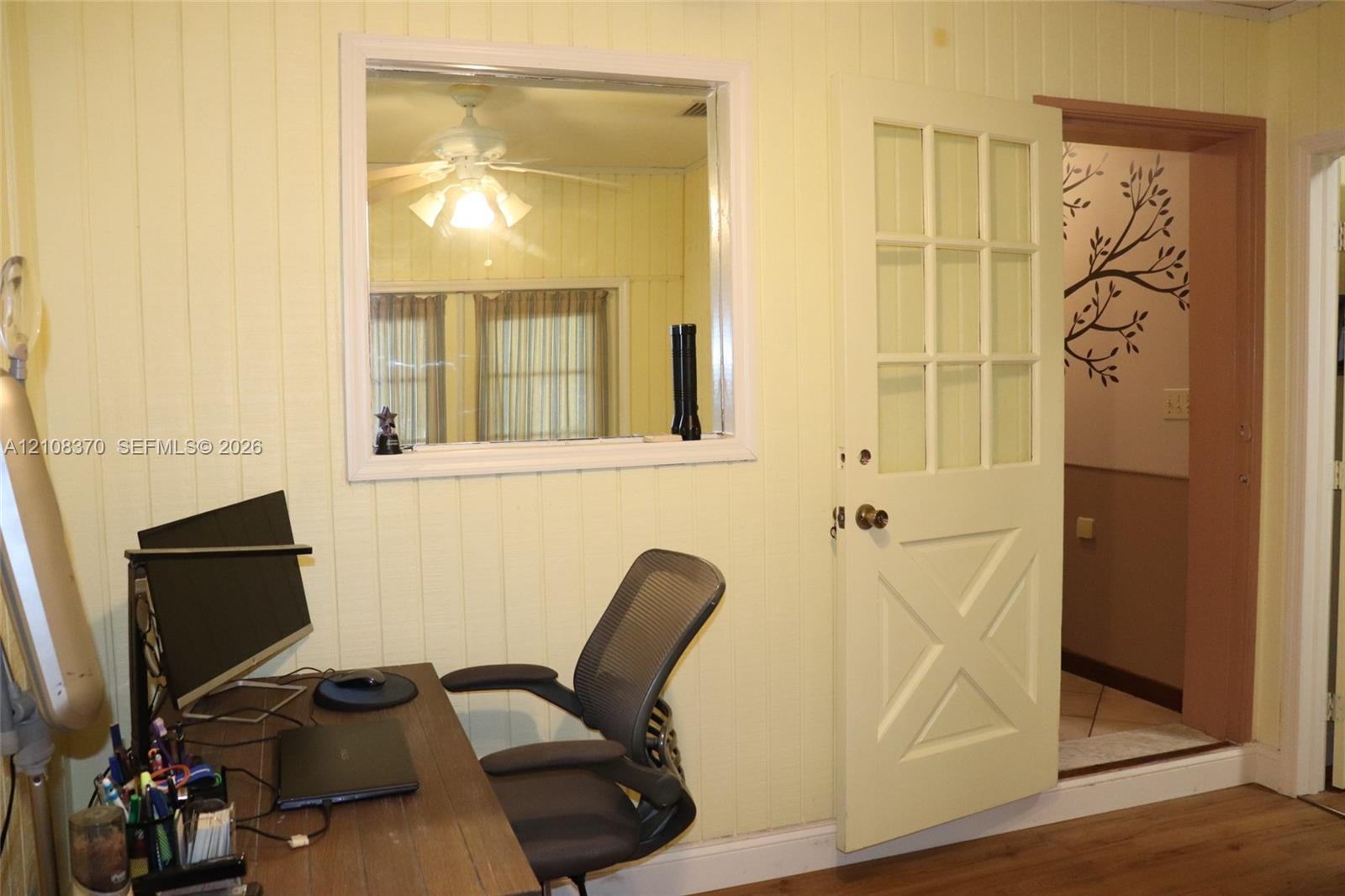 Vertical wood-panel walls, interior fixed-pane window, nine-pane glass and wood door with cross-buck paneling, and wood-finish flooring