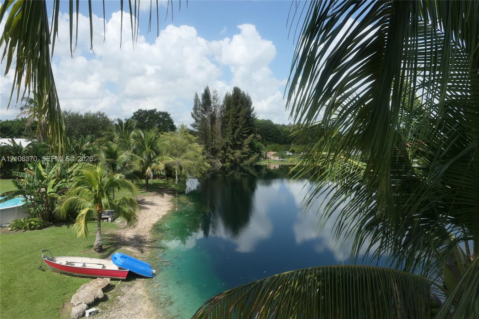 Waterfront property featuring a private shoreline, expansive grassy lawn, and mature palm trees