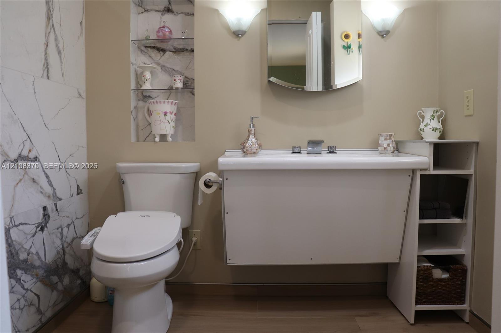 Wall-mounted sink with integrated storage, full-height stone-patterned tile wall, recessed shelving, and dual wall-mounted light fixtures