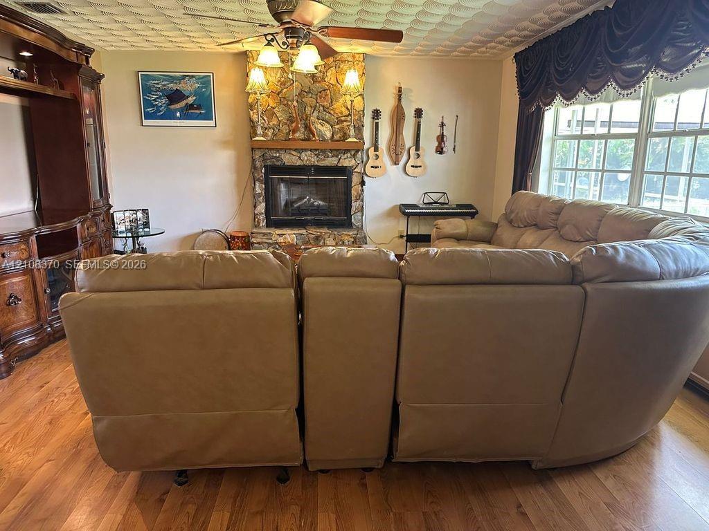 Floor-to-ceiling stone fireplace featuring a wood mantel, integrated wood-finish cabinetry, wood-finish flooring, and a ceiling-mounted light fixture with a fan
