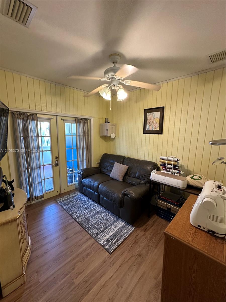 Vertical wood-paneled walls, wood-finish flooring, double-lite glass doors, and a ceiling fan with integrated light fixture