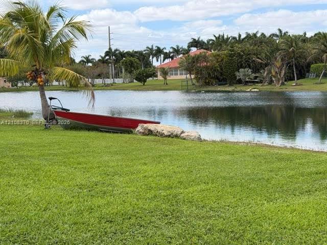 Waterfront lot featuring a manicured lawn, natural pond, boulder accent, and mature palm trees