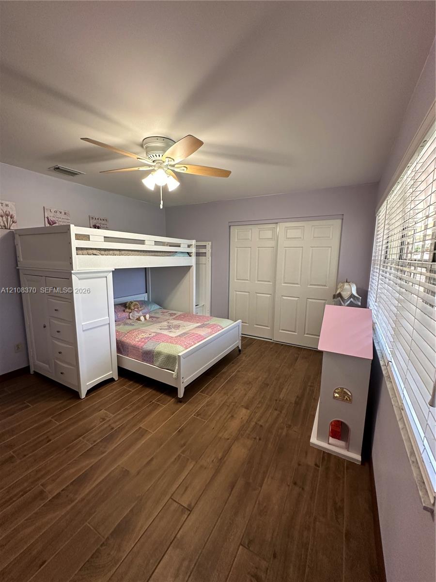 Wood-finish plank flooring, ceiling fan with integrated light fixture, and dual-panel sliding closet doors