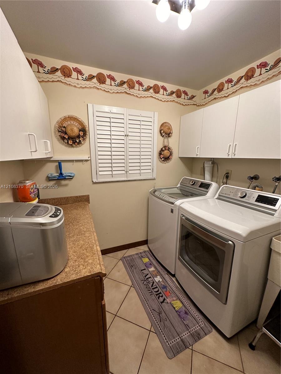 Laundry room featuring white shaker-style wall cabinetry, a laminate countertop, tile flooring, and a window with plantation-style shutters