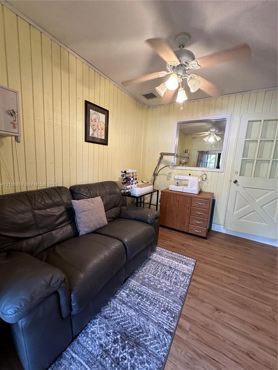 Vertical wood-plank wall paneling, light-toned wood-finish flooring, ceiling fan with integrated multi-light fixture, and a multi-pane door with X-pattern detailing