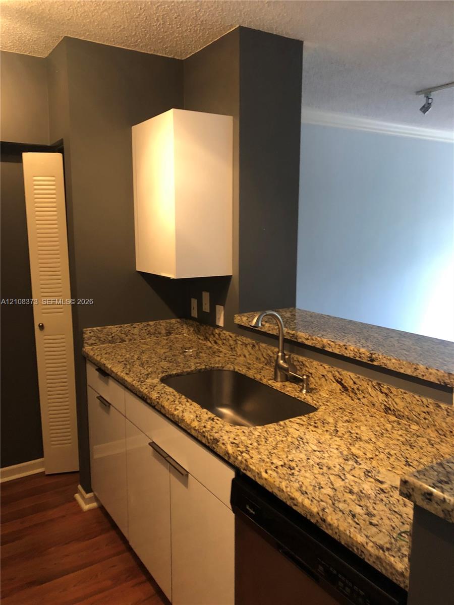 Kitchen featuring stone countertops, stainless steel undermount sink, gooseneck faucet, high-gloss white cabinetry, and wood-finish flooring