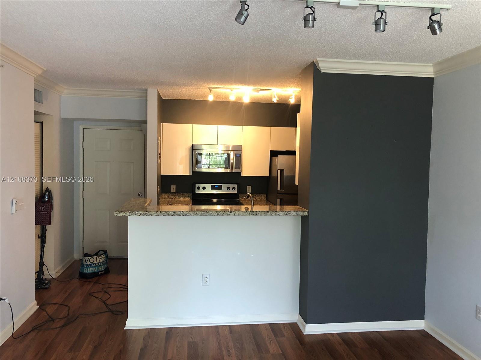 Kitchen featuring white cabinetry, stone-finish countertops, stainless steel appliances, breakfast bar, and adjustable track lighting