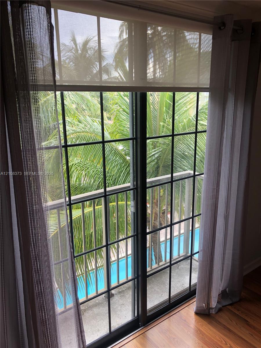 Sliding glass door with a grid pattern, dark-framed balcony with metal railing, wood-finish flooring, and tropical scenery