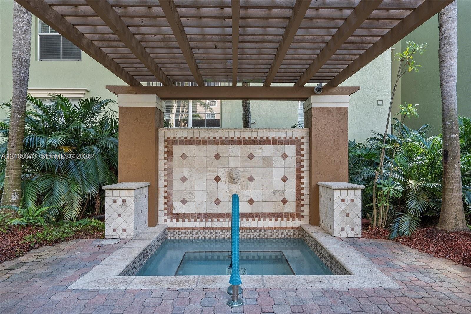 Outdoor spa featuring a stone-tiled wall fountain, wood-slat pergola, and paver stone patio