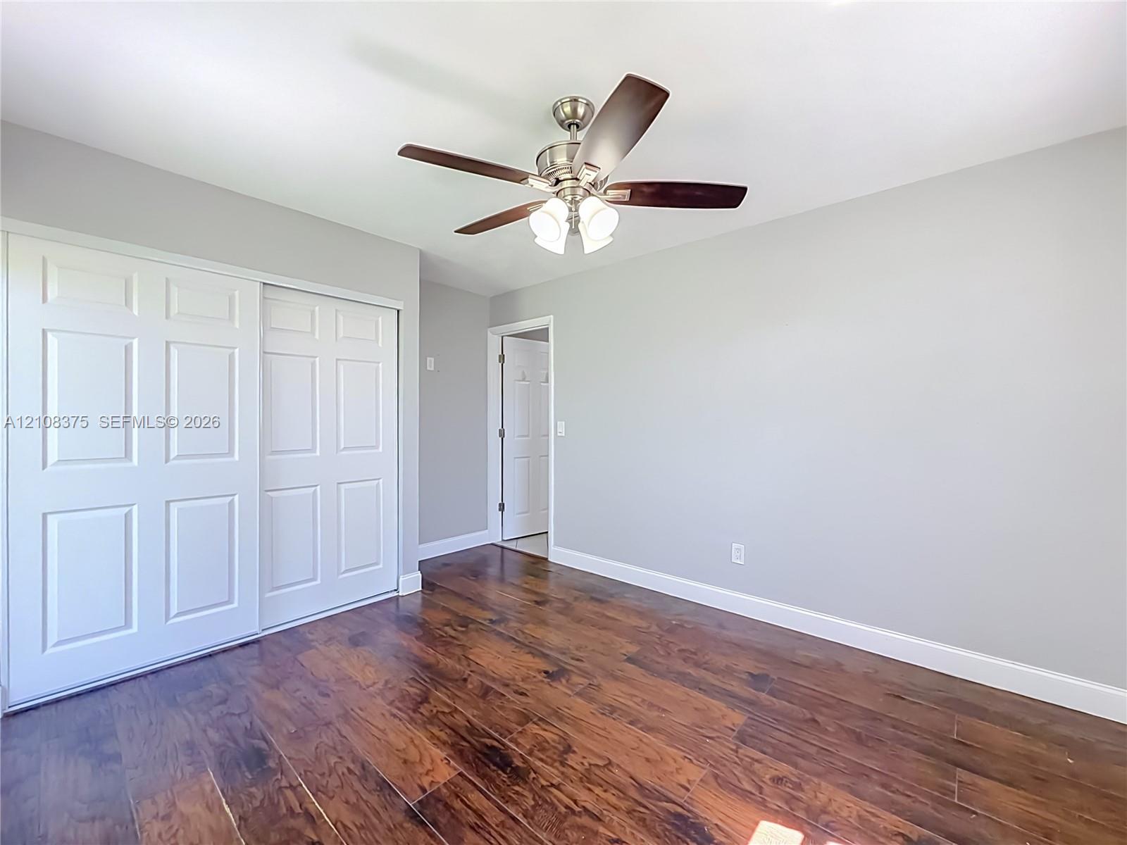 Room featuring wood-finish flooring, a brushed-nickel ceiling fan with a three-light fixture, and a sliding-door closet with white six-panel doors