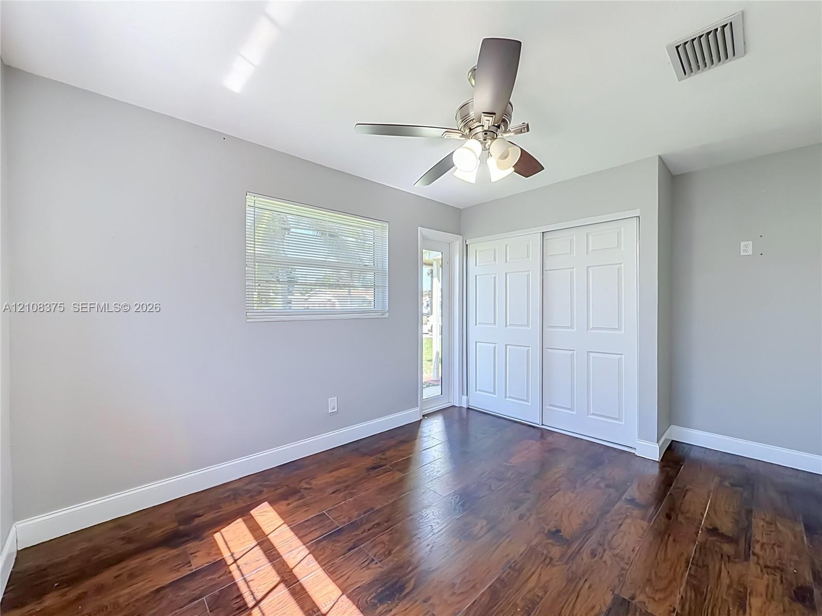 Room featuring wood-finish flooring, a ceiling fan with integrated lighting, a sliding closet with paneled doors, and a glass-paneled exterior door