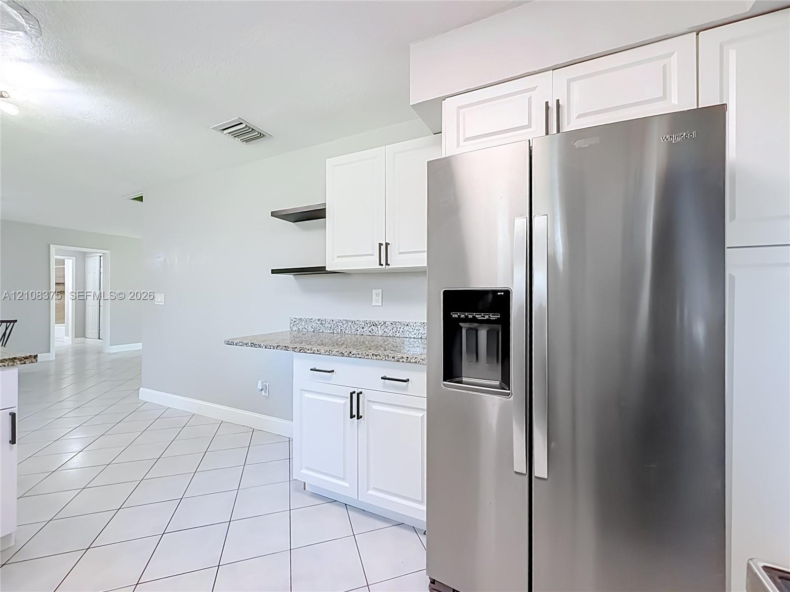 Kitchen featuring white shaker-style cabinetry, stainless steel side-by-side refrigerator, stone-composite countertops, open shelving, and neutral ceramic tile flooring