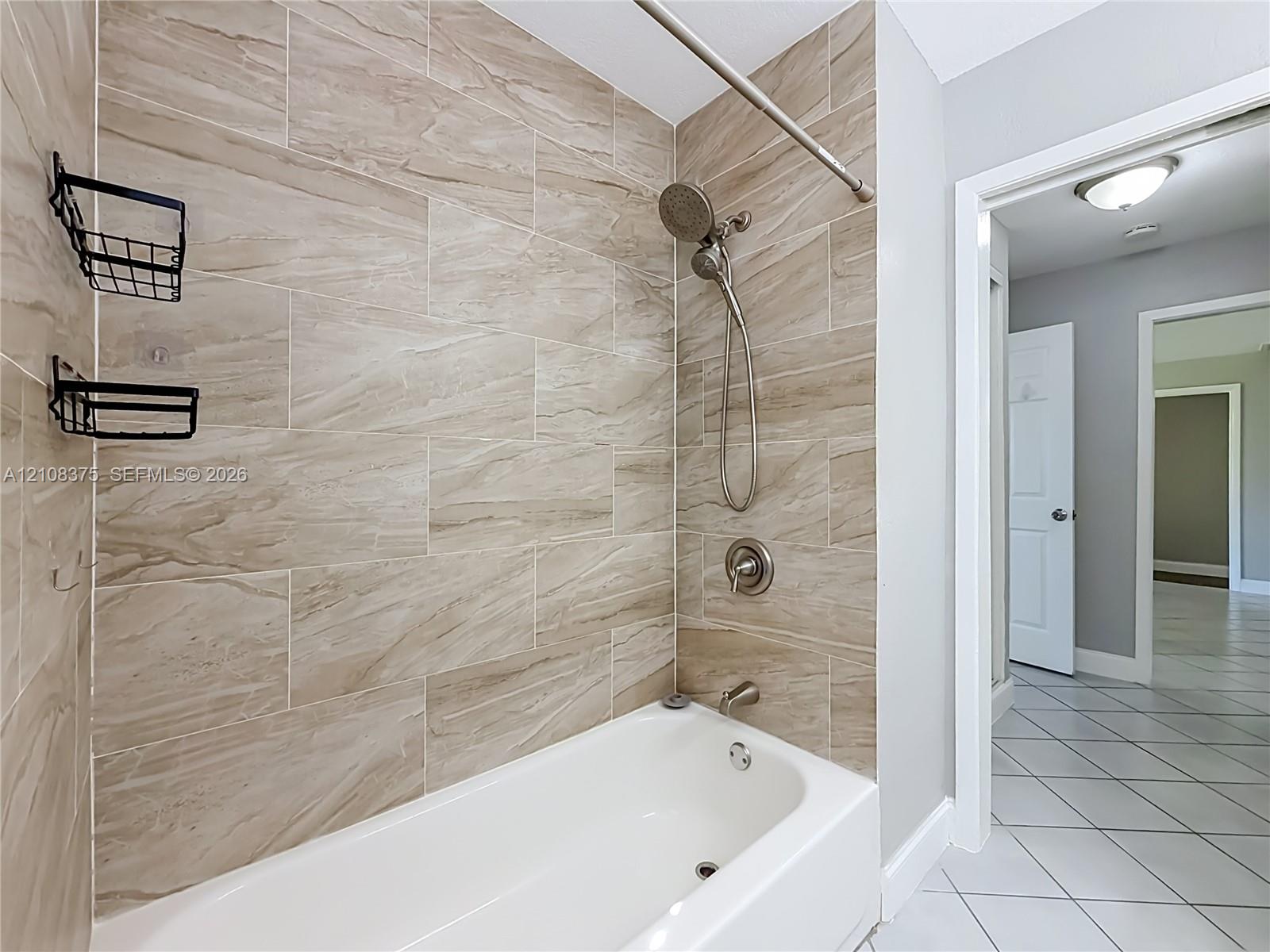 Bathtub and shower combination featuring large-format ceramic tile surround, brushed nickel hardware, and a handheld shower fixture