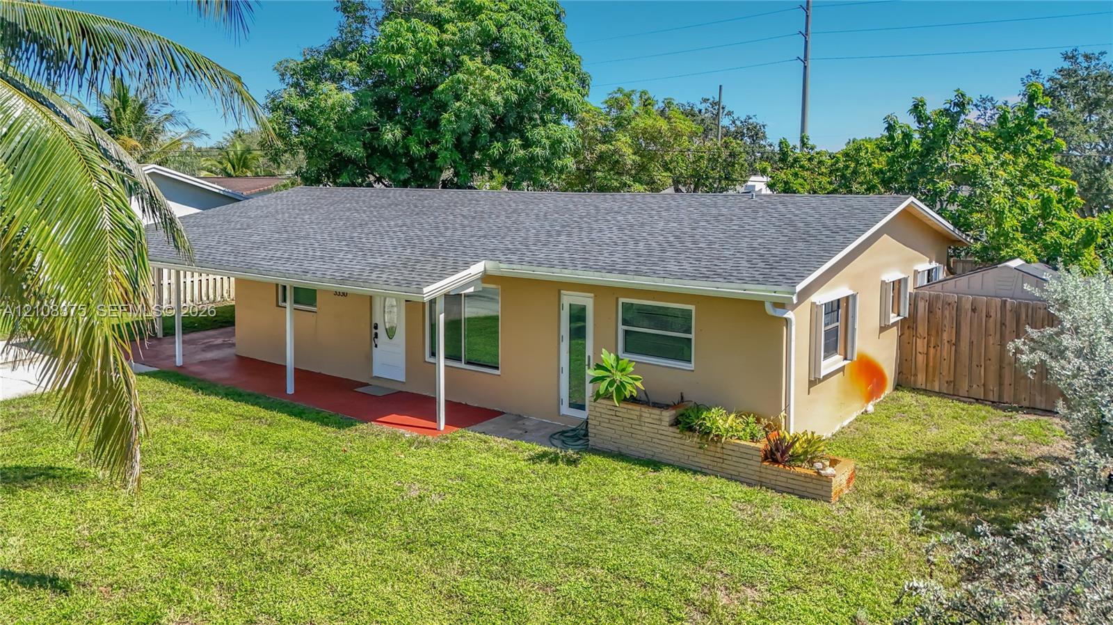 Single-story exterior featuring a covered carport, shingled roof, horizontal siding, masonry planter box, and a fenced backyard