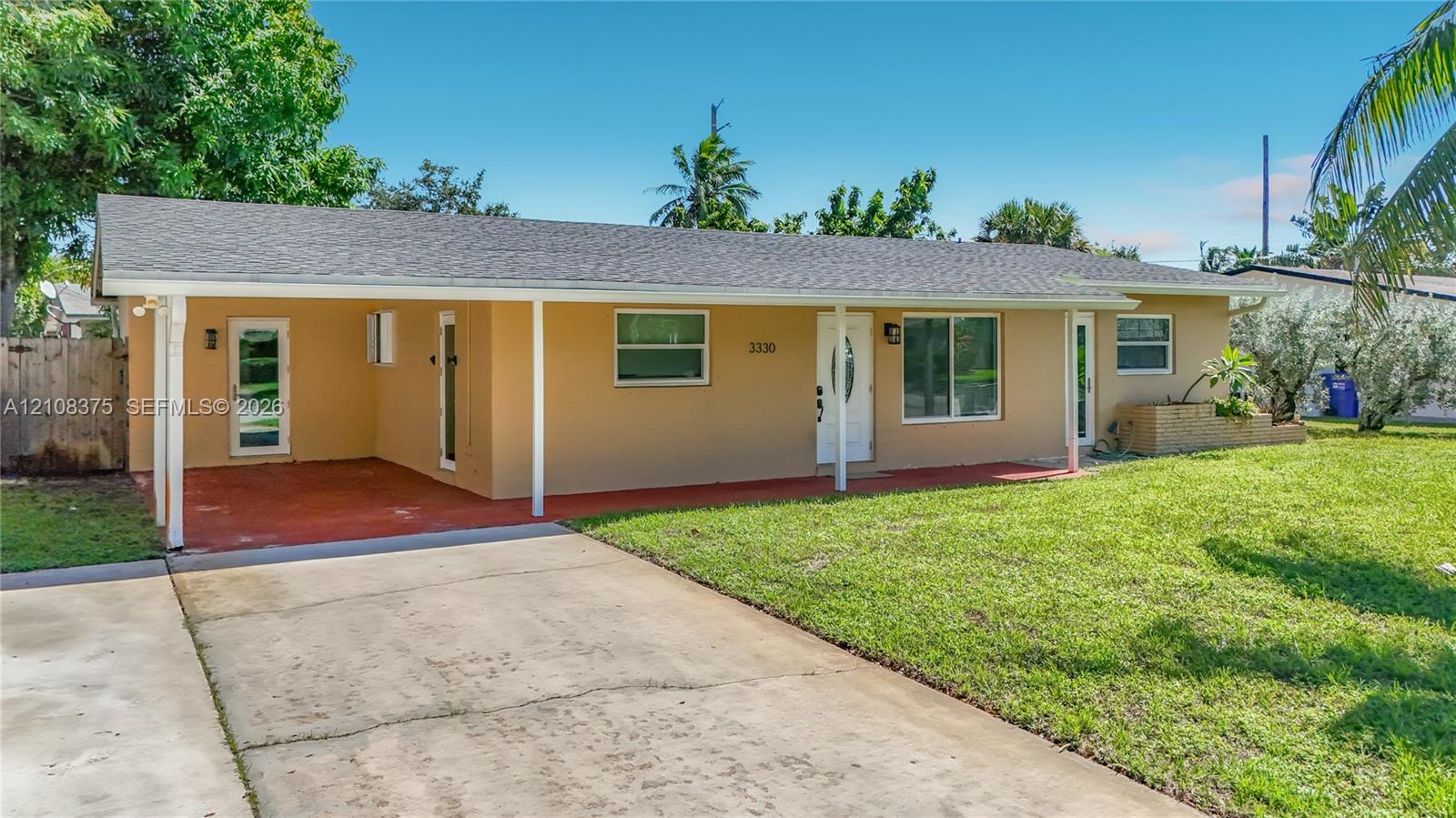 Single-story residence featuring a covered carport, concrete driveway, asphalt shingle roof, and expansive front lawn