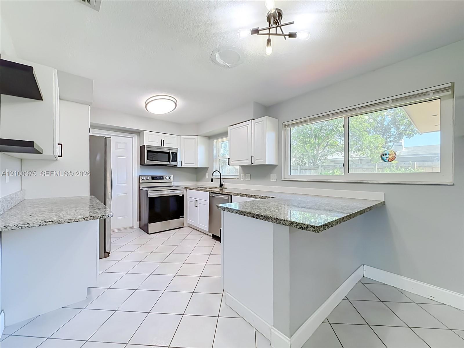Kitchen featuring white cabinetry, stone-finish countertops, stainless steel appliances, a tile floor, and a multi-light chandelier