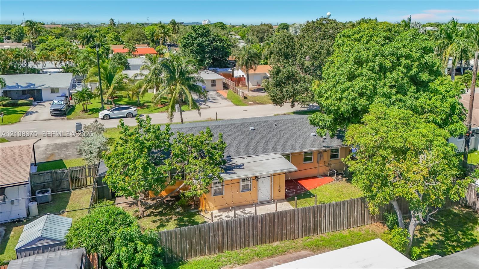 Single-story exterior featuring a shingle roof, concrete patio, perimeter wood fencing, and mature landscaping