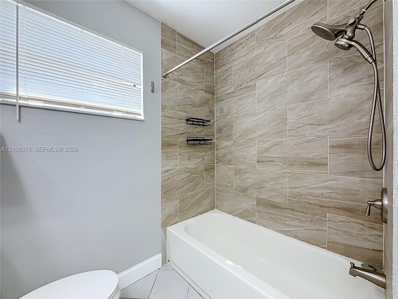 Bathtub featuring large-format ceramic tile surround with natural patterning, brushed-nickel shower hardware, and a horizontal window