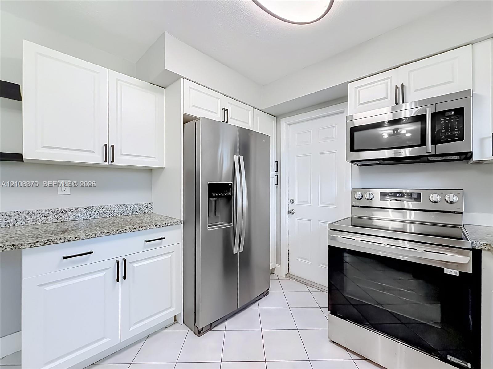 Kitchen featuring white shaker-style cabinetry, stone countertops, stainless steel appliances, and ceramic tile flooring